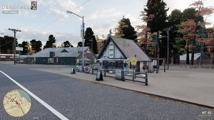 In-engine free-camera view: The BBQ Pit’s A-frame, picnic yard and neighboring Filling Station beside Highway 83 at golden hour. Original minimap and location HUD remain visible.