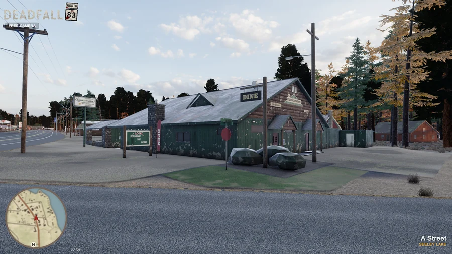 In-engine free-camera view: The Filling Station’s weathered green siding, log gable and Dine sign at golden hour. Original minimap and location HUD remain visible.